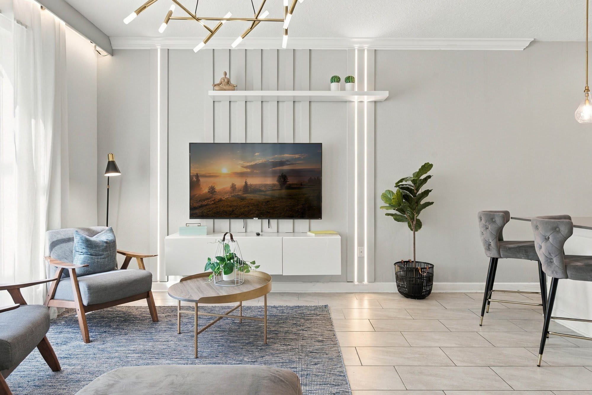 Una sala de estar moderna con un televisor de pantalla plana montado en la pared, una mesa redonda de centro con una planta, dos sillones y una mesita auxiliar.