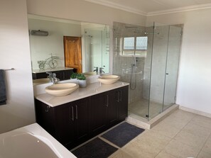 Une salle de bain moderne avec une douche à parois de verre, deux vasques, des meubles sombres et une baignoire.