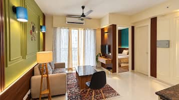 Una habitación de hotel moderna con zona de comedor, sofá, televisor y cama.
