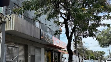 A street view with a tree-lined sidewalk, a closed shop with a metal gate, and parked cars.