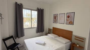 A bedroom with a bed, a nightstand, a chair, a window with curtains, and wall art.