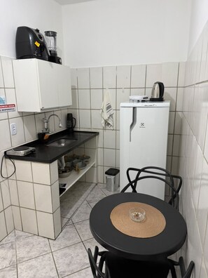 A compact kitchen with a black countertop, a white refrigerator, and a small dining table with chairs. - Apartamento aconchegante (Vitória)