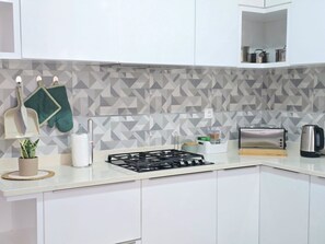 Una cocina moderna con armarios blancos, estufa a gas, hervidor y tostadora.