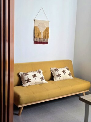 Un sofá con dos almohadones, un tapiz colgado en la pared y un suelo de madera.