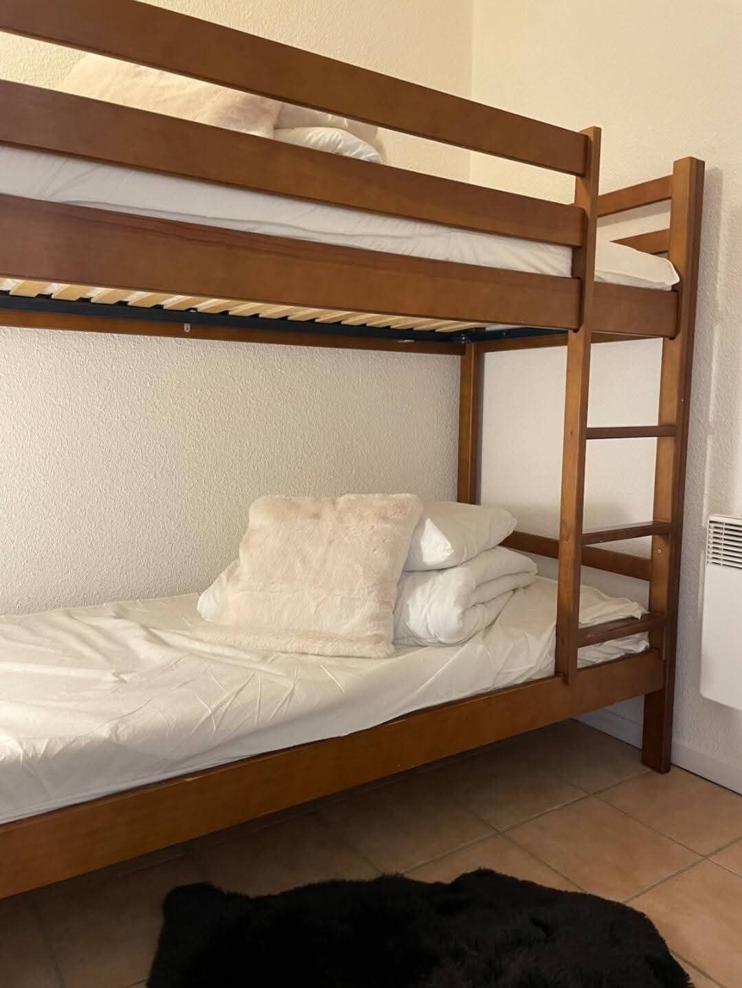 Una cama litera con escalera, ropa de cama blanca y una alfombra negra.