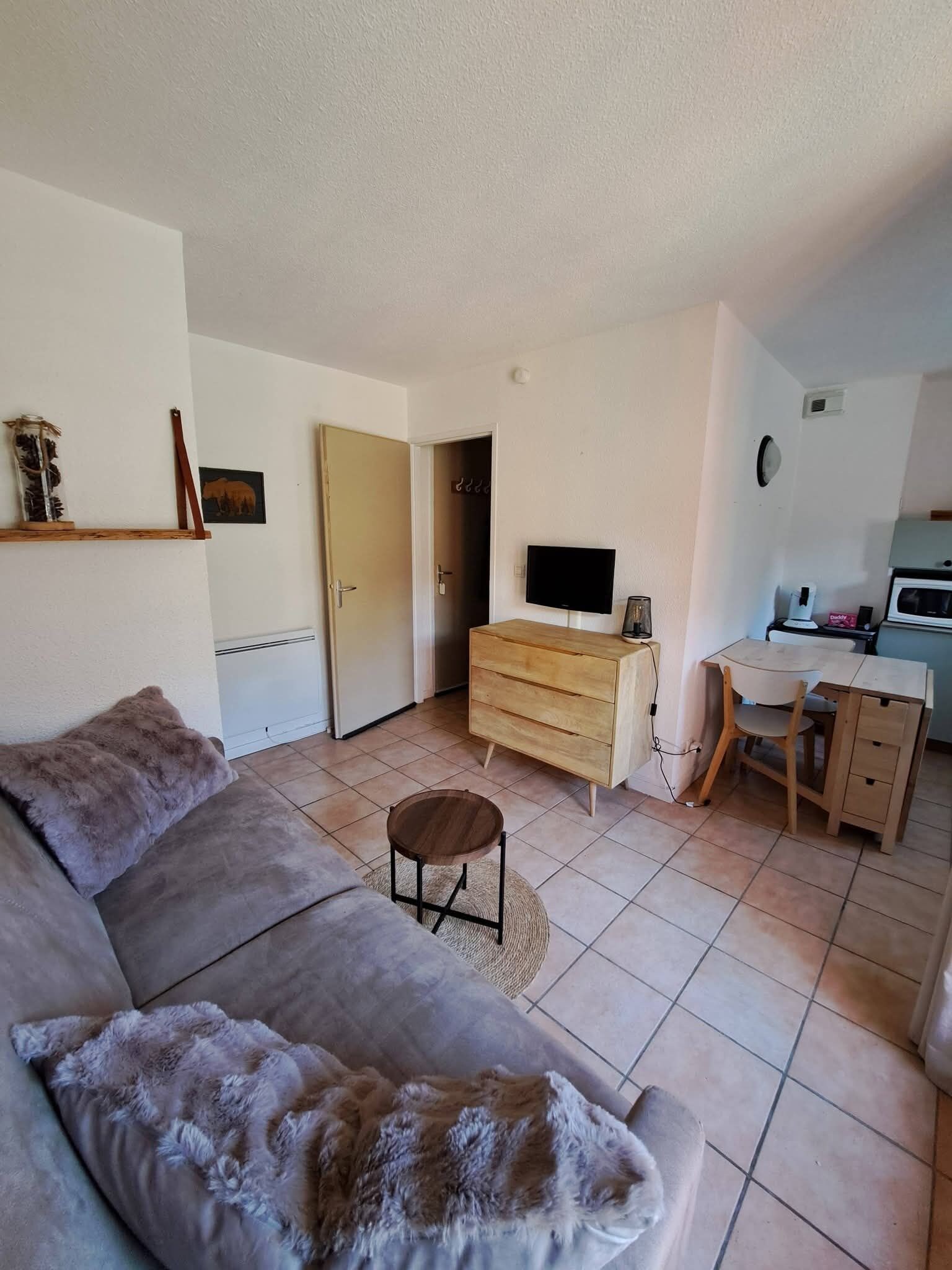 Un salon comprenant un canapé, un téléviseur, une commode en bois et un coin cuisine avec un four à micro-ondes.