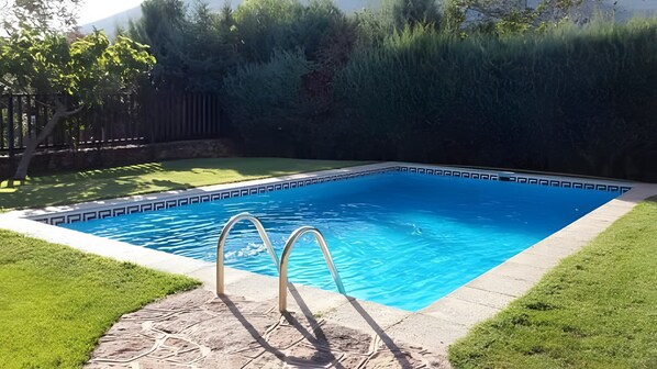 Una piscina rectangular con superficie de agua azul cristalina, rodeada por una solana de piedra y una zona de césped.