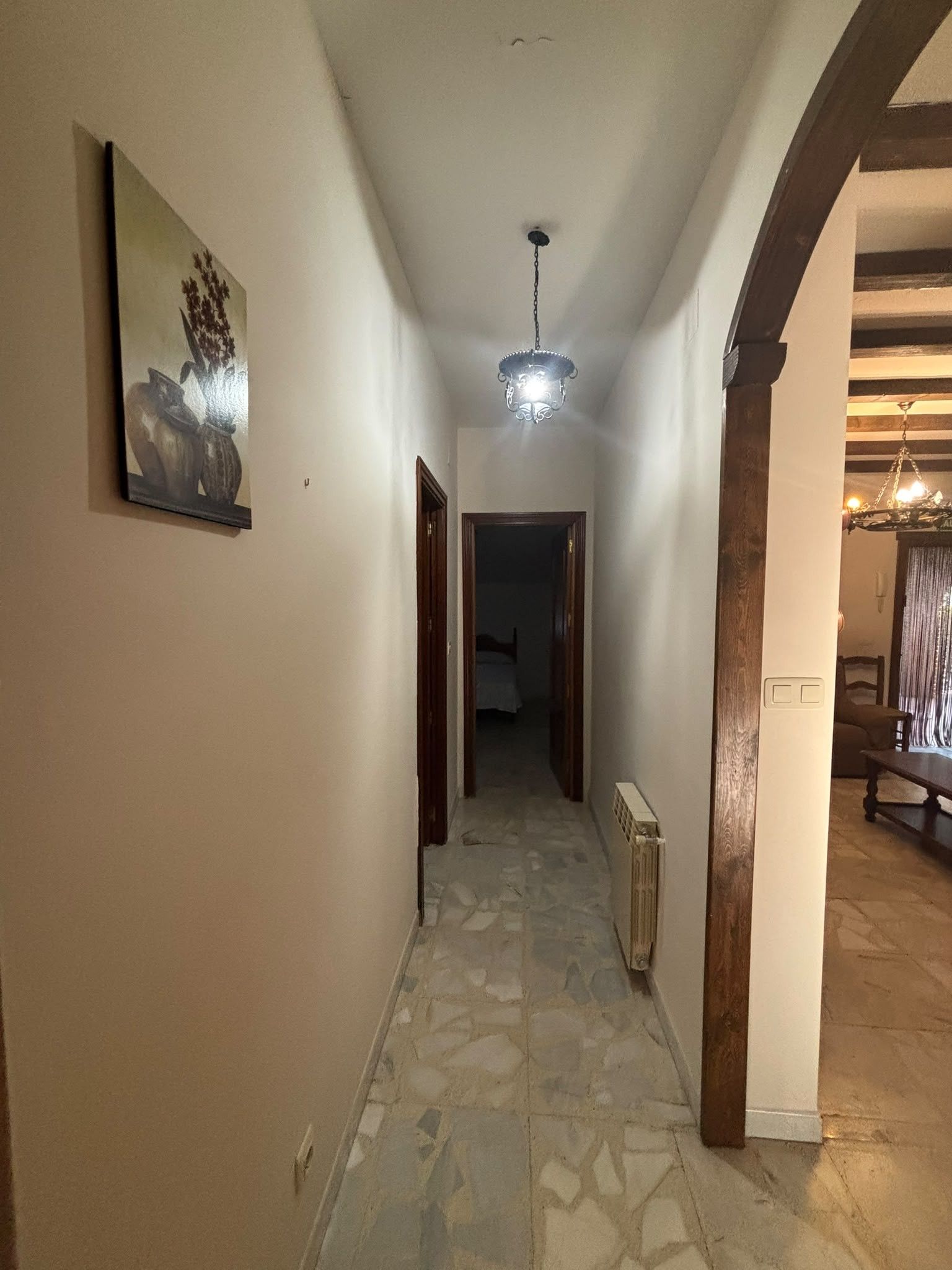 Un pasillo con un radiador, una lámpara en el techo y una puerta que da a otra habitación.