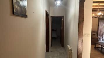 Un pasillo con un radiador, una lámpara en el techo y una puerta que da a otra habitación.