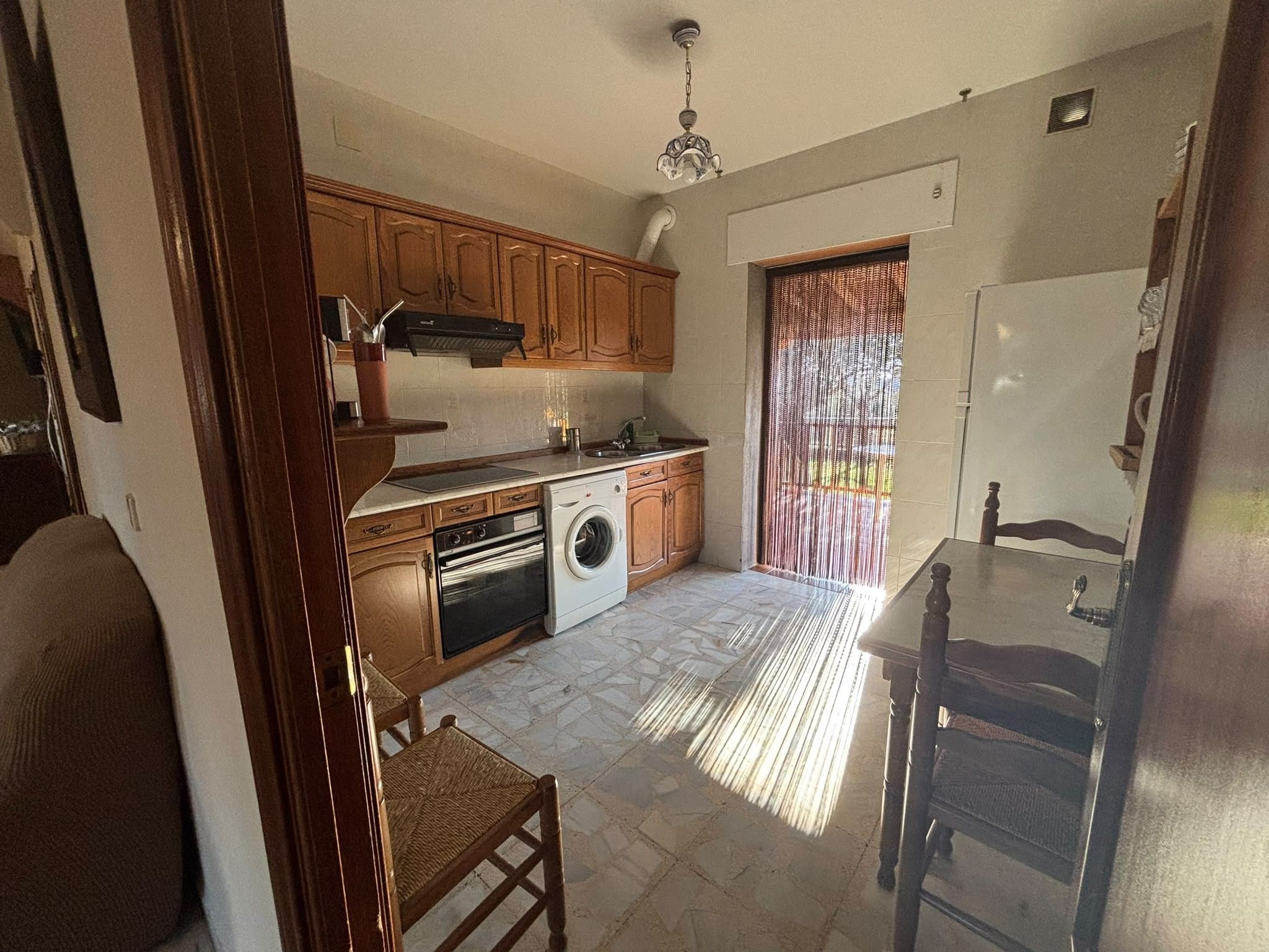 Cocina compacta con armarios de madera, lavadora y comedor con mesa y sillas.