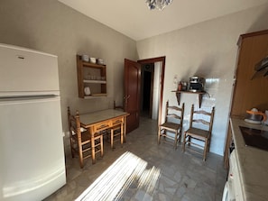 Una cocina compacta con refrigerador, mesa de madera, sillas y una cafetera.