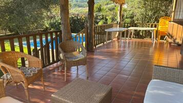Una veranda coperta con mobili in vimini, un tavolo e vista su una piscina e vegetazione.