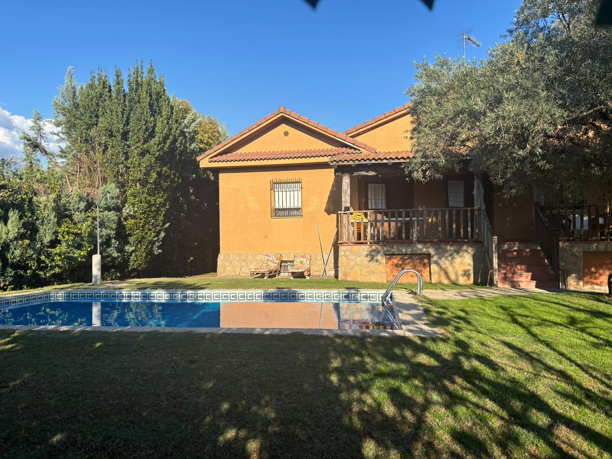Una casa a due piani con piscina, una scala in pietra e un balcone.