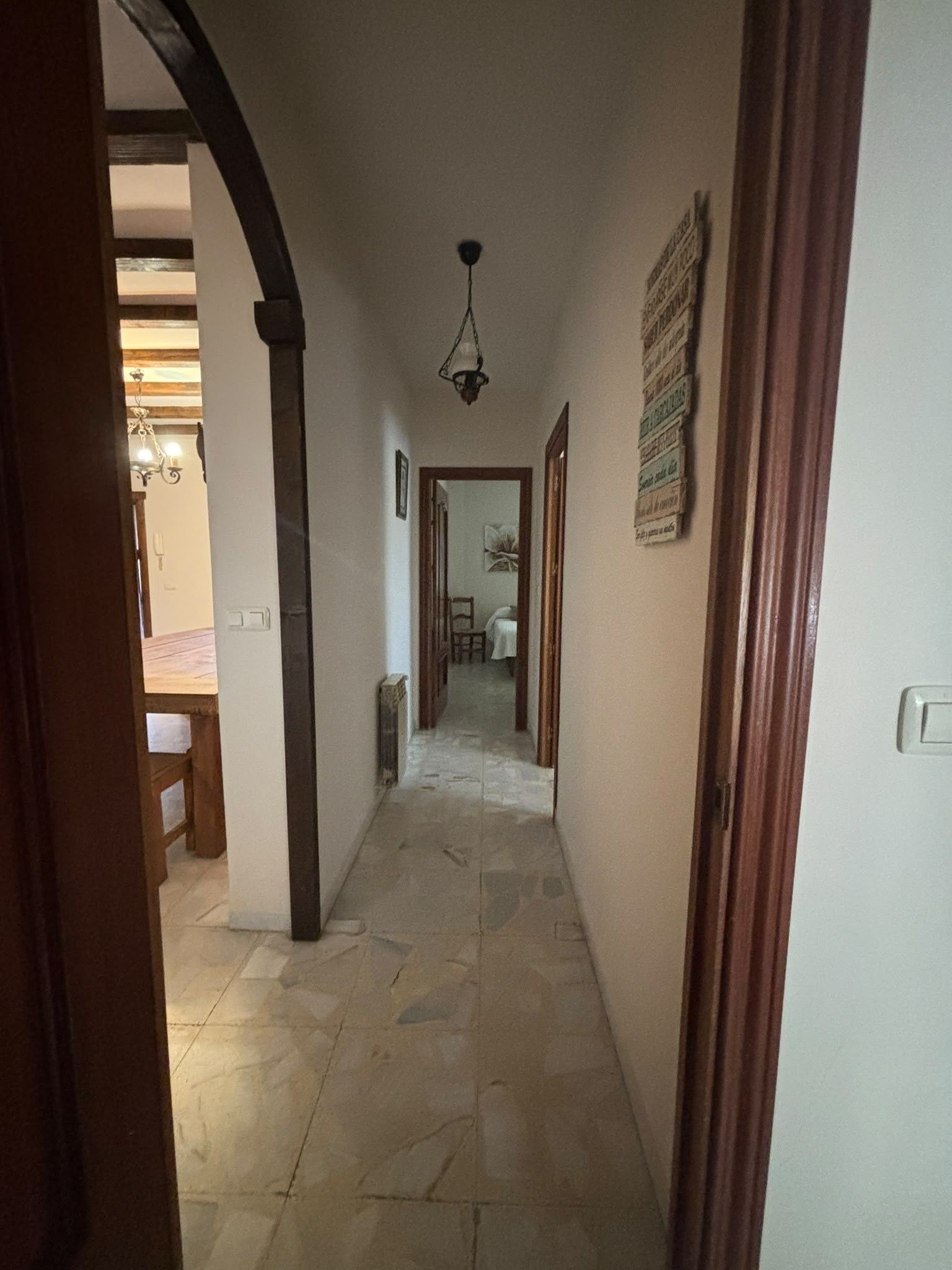 Un pasillo con piso de piedra, marcos de madera y una lámpara colgante.