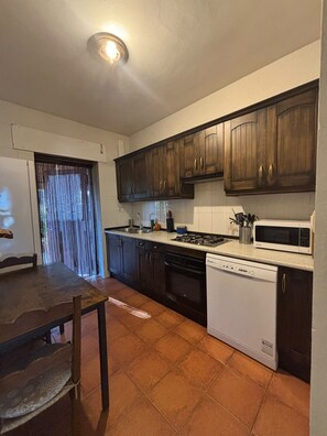 Una cocina con armarios de madera oscura, un lavavajillas blanco, un microondas y piso de baldosas.