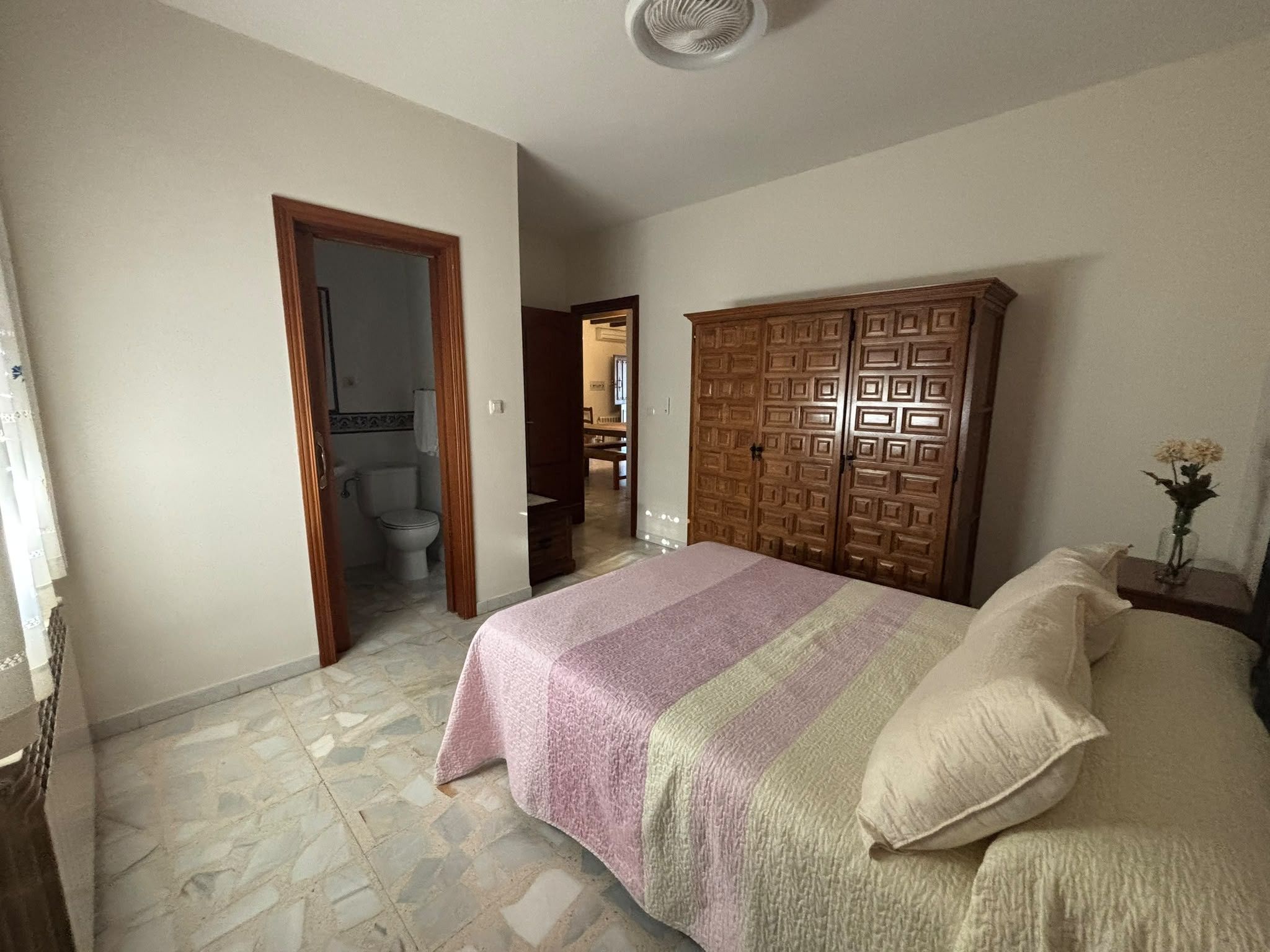 Una camera da letto con un letto, un armadio in legno e un bagno visibile attraverso una porta aperta.