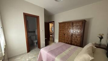 Una camera da letto con un letto, un armadio in legno e un bagno visibile attraverso una porta aperta.