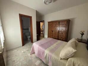 Una camera da letto con un letto, un armadio in legno e un bagno visibile attraverso una porta aperta.