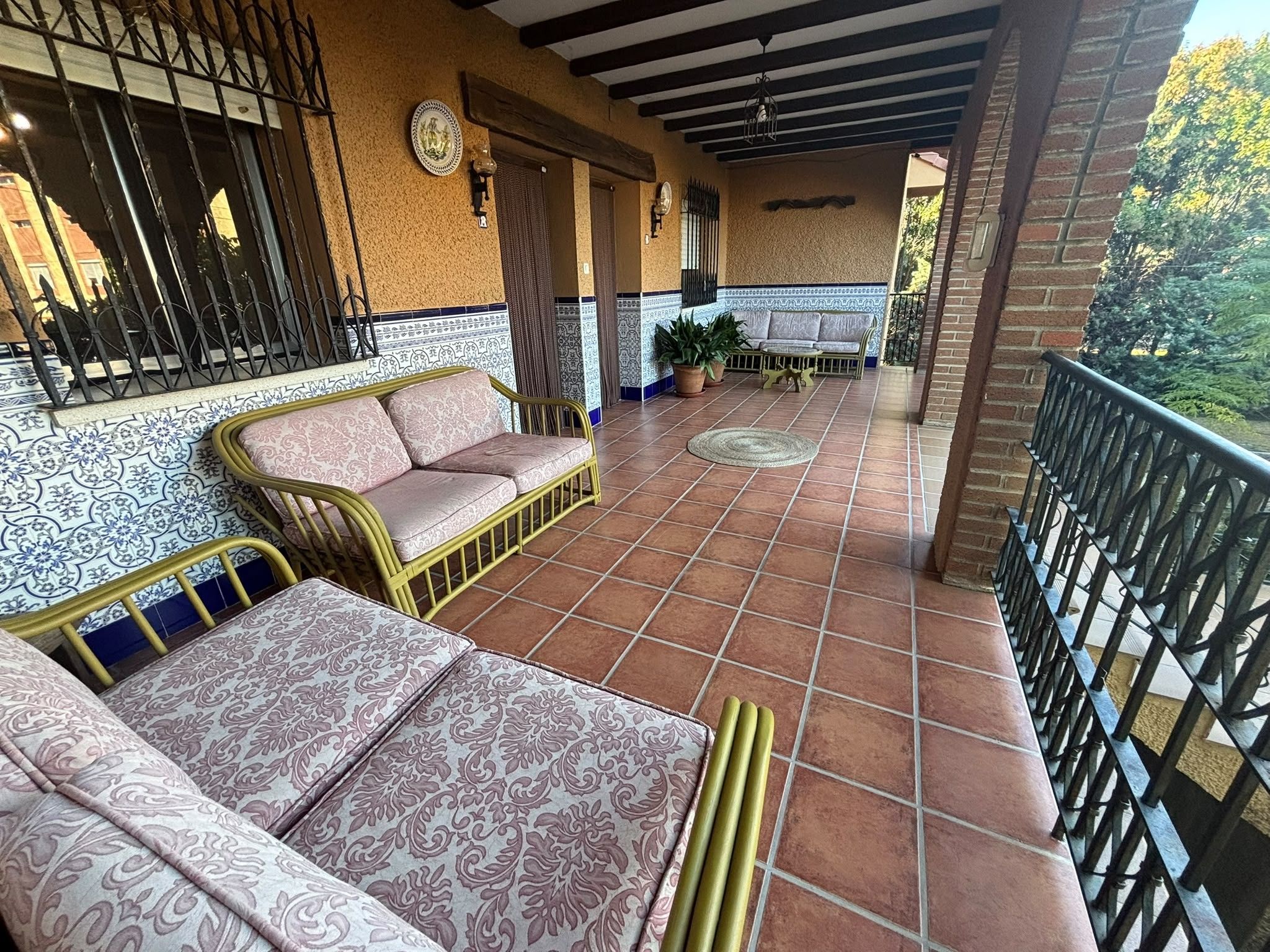 Une terrasse couverte avec un canapé et une table, un sol carrelé et une rambarde.