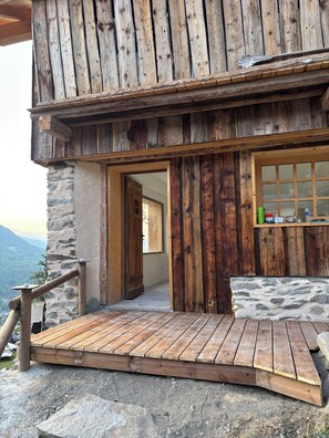 Un bâtiment rustique en bois, avec une façade en pierre, une terrasse en bois et une vue sur les montagnes.