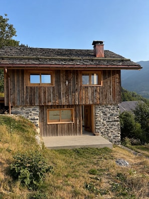 Une maison en bois à deux étages, avec des murs en pierre, de grandes fenêtres et une cheminée.