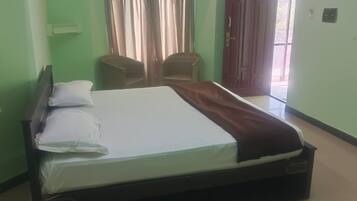 Una cama individual con almohadas y una manta, dos sillas de mimbre, una puerta y un interruptor de luz en la pared.