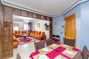 A dining area with a table set for four, a sofa, and a TV in the background. - Majorelle FAMILY RESIDENCE (Marrakech)