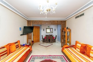 A hotel room with two sofas, a TV, a chandelier, a dining table with chairs, and a cabinet. - Majorelle FAMILY RESIDENCE (Marrakech)