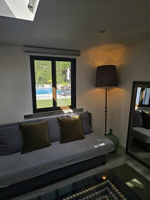 Un salon moderne avec un canapé, une lampe sur pied et une grande fenêtre donnant sur une piscine.