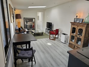 Un espace de vie compact comprenant un coin repas, un téléviseur, un meuble avec des portes en verre et une petite cuisine.
