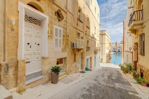 Uma rua estreita com edifícios tradicionais, uma porta branca e um vaso de planta.