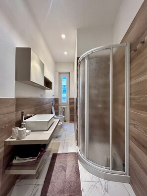 A modern bathroom with a glass shower enclosure, a large sink, and a mirror above the vanity.