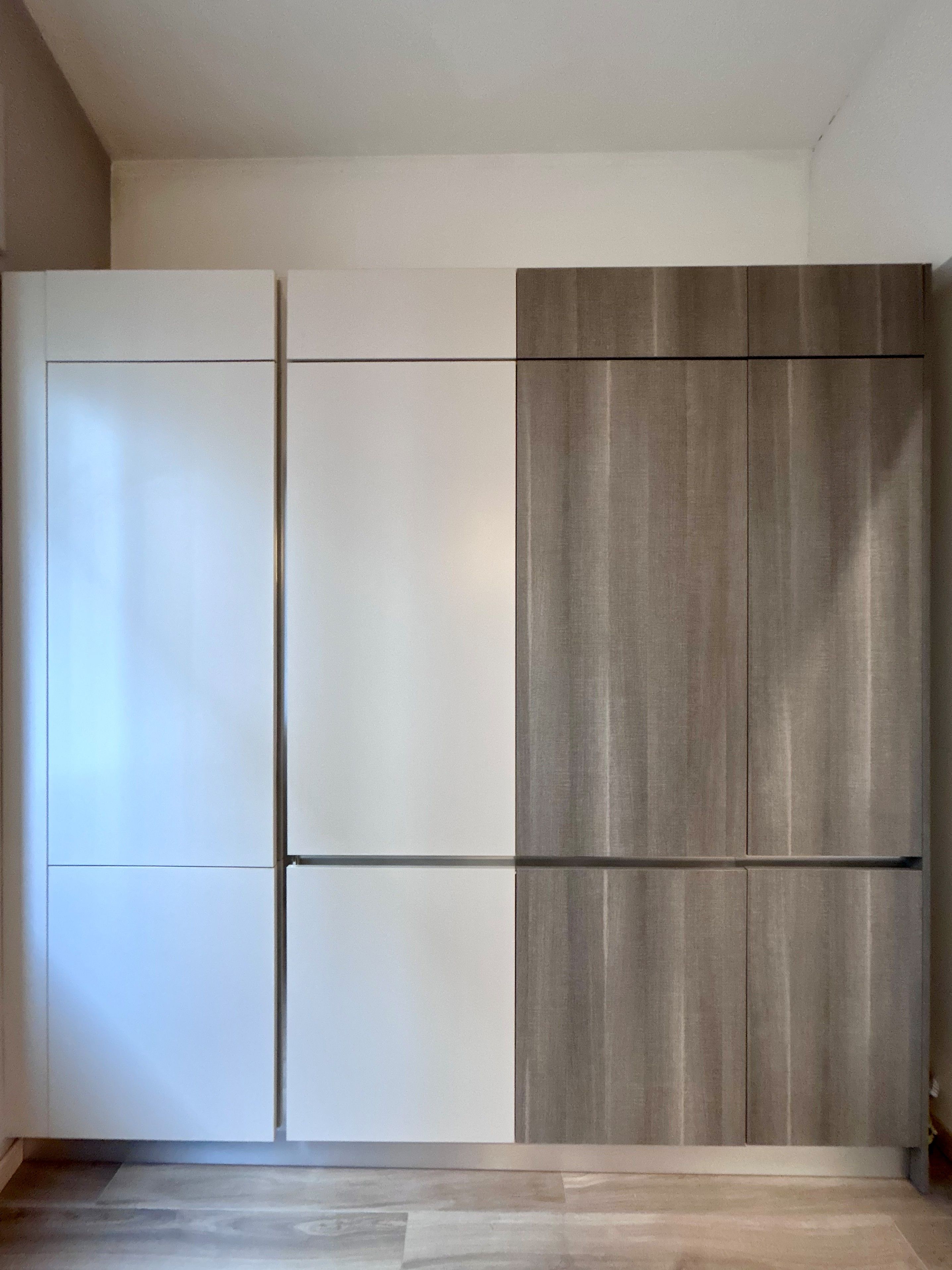 A room with a large wardrobe, a wooden floor, and a plain wall.