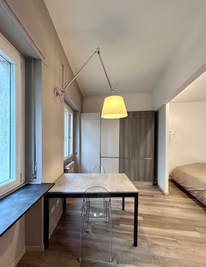 A modern interior with a dining table, chairs, a pendant light, and a bed.