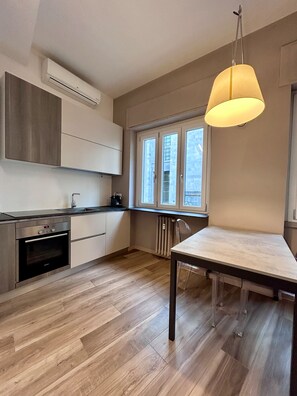 A modern kitchen with a built-in oven, a dining table, and a hanging light fixture.