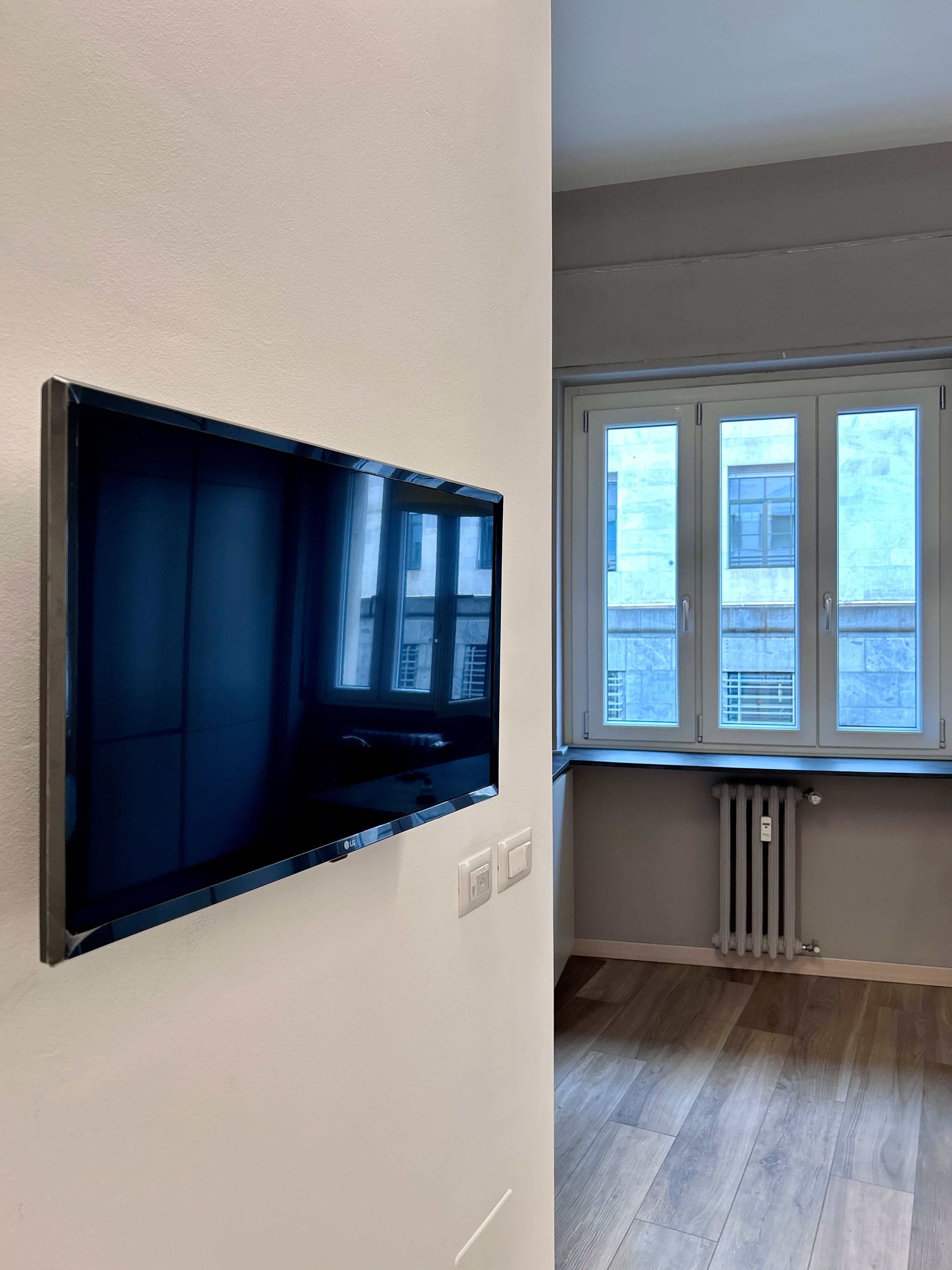 Ein Zimmer mit einem an der Wand befestigten Flachbildfernseher, einem Fenster mit Jalousien und einer Heizung.