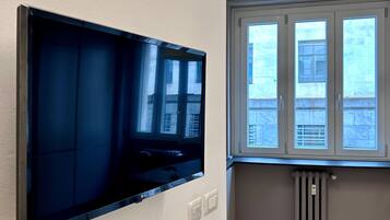 Ein Zimmer mit einem an der Wand befestigten Flachbildfernseher, einem Fenster mit Jalousien und einer Heizung.