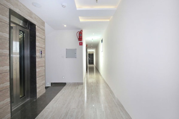 A hallway with a marble floor, a fire extinguisher mounted on the wall, and a digital elevator control panel. - Hotel O TAJ STARS (Zirakpur)