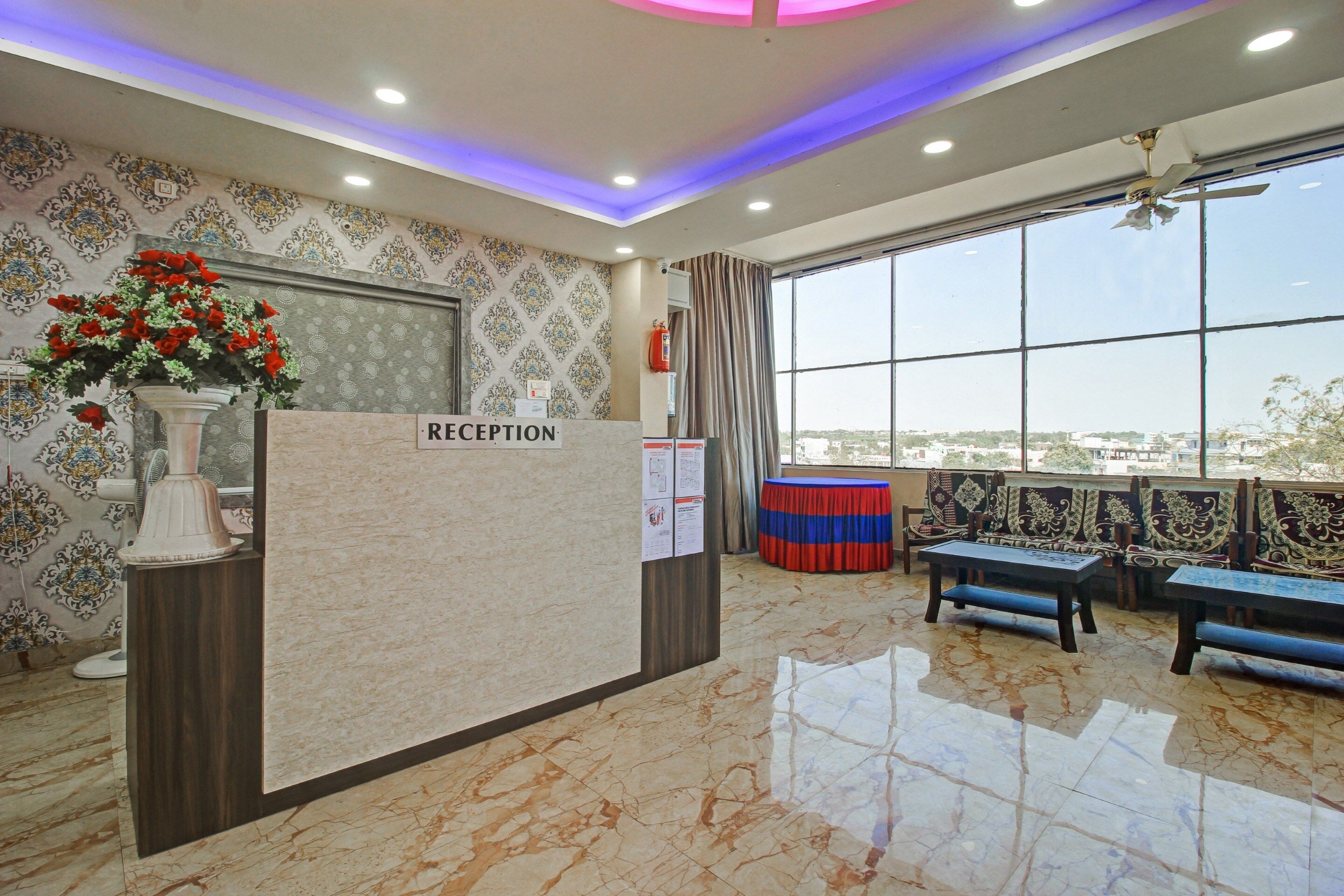 A reception area with a marble floor, a reception desk labeled 'RECEPTION', a large window with a view, and a seating area with patterned cushions.