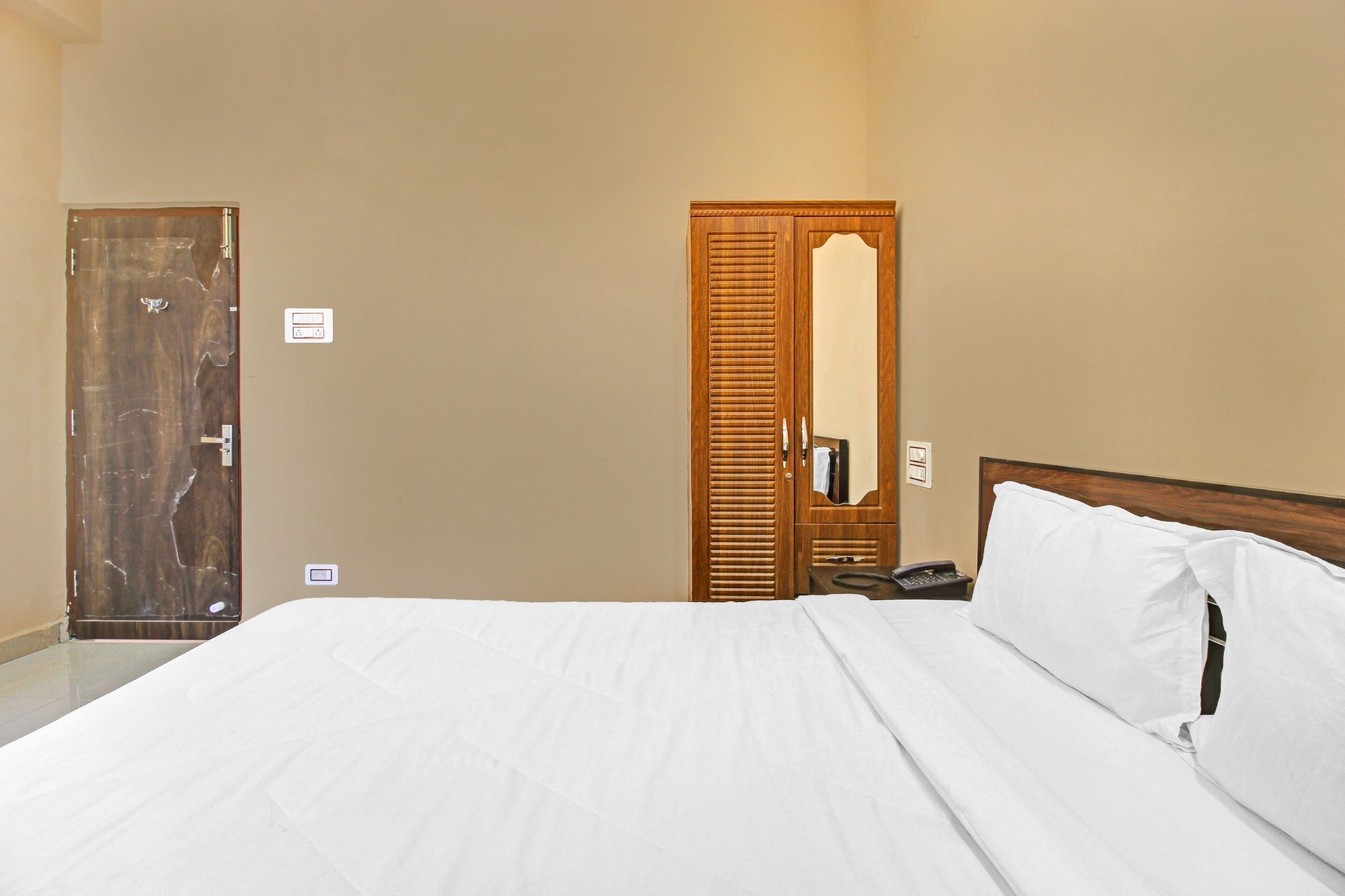 A hotel room with a bed, a wooden door, a mirror, and a telephone.
