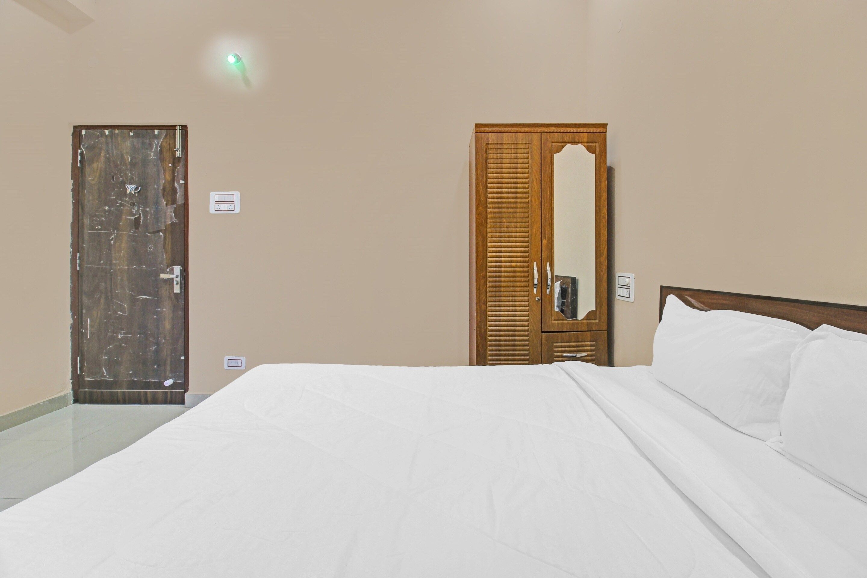 A hotel room with a bed, a wooden wardrobe, a mirror, and a door.