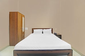 Una cama individual con ropa de cama blanca en una habitación con un armario de madera y una mesita de noche con teléfono.