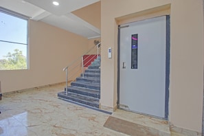 Un pasillo con piso de mármol, una escalera con barandillas de metal y una puerta con manija.