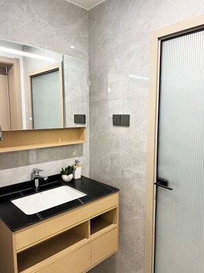 Un baño moderno con lavamanos de encimera negro, un espejo y una puerta con pomo vertical.
