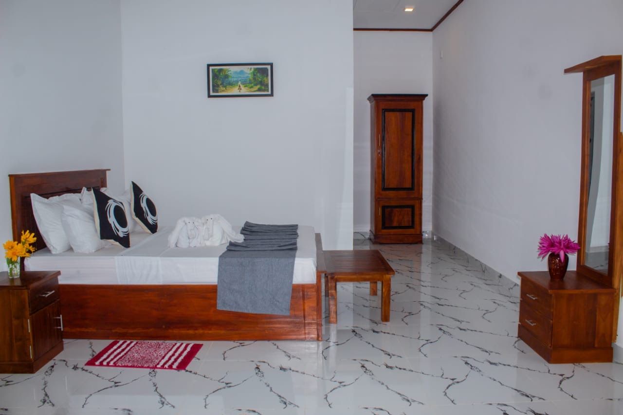 Une chambre à coucher avec un lit en bois, une table de chevet, une commode, un tapis rouge et blanc, une armoire en bois et un miroir.