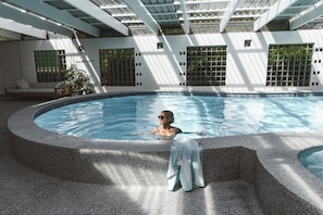 Piscina com uma pessoa na água, área de estar com sofá e planta em vaso.