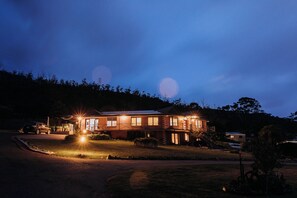 Uma casa de dois andares com uma entrada frontal bem iluminada, uma entrada de carros e um gramado.