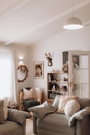Uma sala de estar acolhedora com um sofá, poltronas, uma estante de livros e uma cabeça de veado decorativa.