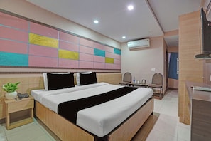 Quarto de hotel com cama, mesa de cabeceira e parede com padrão geométrico colorido.