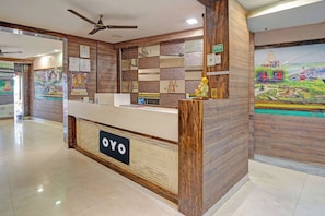 Uma receção com uma placa a indicar 'OYO' num hall de hotel com lambris e um mural na parede.